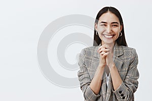 Horizontal shot of stylish happy european girlfriend in jacket, clasping hands together over chest and smiling joyfully photo