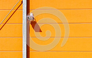 Horizontal shot of a track light on a bright orange wall during daylight
