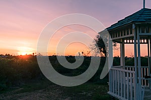 Horizontal shot of a white gazebo pavilion structure in a green grassy field during sunset