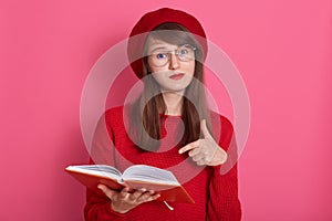 Horizontal shot of woman with orange note book pointing at its pages with her index finger. Attractive female wearing red sweater