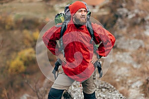 Horizontal shot of young male hiking in mountains wearing red clothes, looks away. Traveler bearded man relaxing after trekking