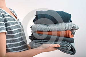 Horizontal shot of a Girl teenager holding a pile of clothes, isolated on gray background