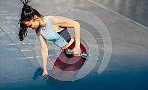 Horizontal side view of an athlete woman doing exercises with dumbells outdoors