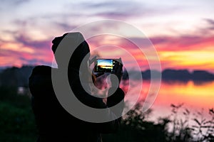 Horizontal silhouette photo of girl taking sunset photo on smartphone