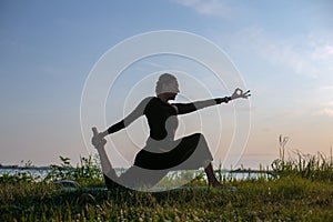 Horizontal silhouette photo of a slender woman doing yoga outdoors at sunset