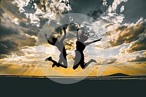 Horizontal silhouette of two friends jumping high under the breathtaking cloudy sky during sunset