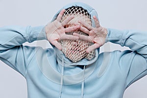 horizontal studio photo of a strange, tortured man in a light blue hoodie covering his face with his hands, standing on