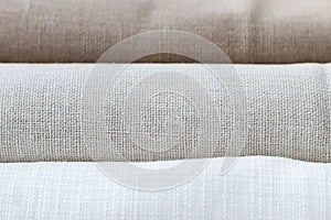 Horizontal textural background of three types of natural linen fabric, rolled up. Selective focus. Closeup view