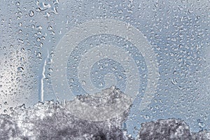 A horizontal texture of water droplets and melting snow and ice is on the glass and on a background of blue sky