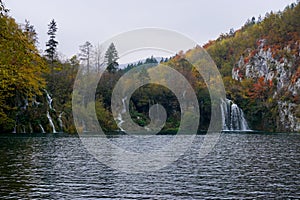 Horizontal view of calm lake with a waterfall and colorful fall foliage