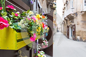 Horizontal View of Close Up of a Composition of Flowers in a Yellow Wooden Box Hanged on a Door in a Street. Taranto, South of It