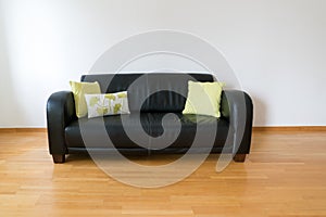 Horizontal view of a dark brown leather couch with three pillows in a minimalist apartment