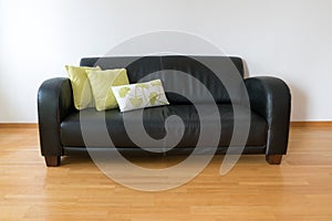 Horizontal view of a dark brown leather couch with three pillows in a minimalist apartment