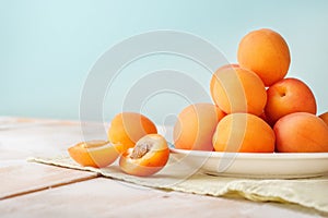 Horizontal view of Delicious ripe orange apricots in a bright plate on wooden table with green napkin on light blue wall