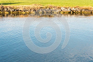 Horizontal view of a river canal with deep blue water and a rocky edge and green grass behind abstract view