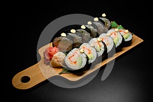 Horizontal view of sushi roll futomaki with avocado and crab meat on wooden serving board on black background.