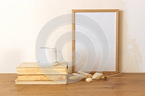 Horizontal white frame mockup on a vintage wooden bench, table, ceramic mug, and saucer with dry Lagurus ovatus grass. White wall