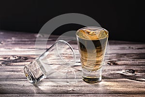 Horizontally oriented chopped view of a shot of whiskey or scotch or bourbon next to a second dropped shot