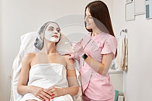 Horizontalshot of beautiful woman receiving spa treatment. Cosmetologist in beauty salon cleaning woman`s face, applying cream