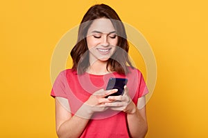 Horizontalshot of smiling woman holding mobile phone and text messaging, looking at her device`s screen and smiling happily,