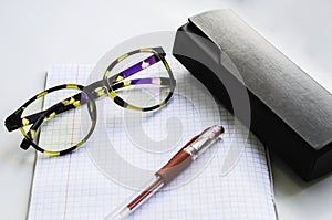 Horn-rimmed glasses, red ink pen and glasses case on a checkered notebook photo