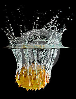 Horned melon falling into water splash in a black background