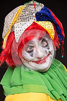 A horrible clown with a terrible make-up and hat laughing on a b