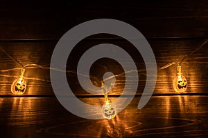 Horrible symbol of Halloween - Jack-o-lantern garland with three orange pumpkins. Scary head of pumpkin glowing inside on dark