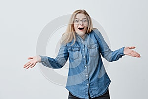 Horrified woman with blonde hair and eyeglasses gestures in puzzlement, being shocked, surprised as remembers that she