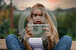 Horrified young woman staring wide-eyed at her tablet