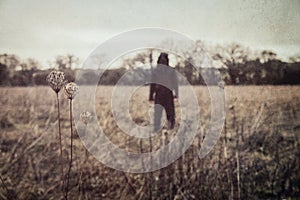 A horror concept of a hooded figure. Standing in the countryside. With a grunge, vintage edit
