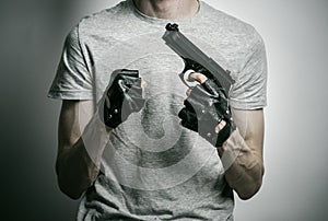 Horror and firearms topic: the killer with a gun in his hand in black gloves on a gray background in the studio