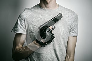 Horror and firearms topic: the killer with a gun in his hand in black gloves on a gray background in the studio