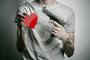 Horror and firearms topic: suicide with a gun in his hand and a red heart on a gray background in the studio