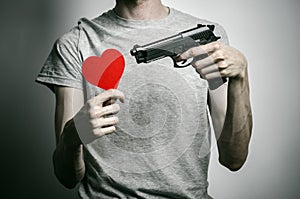 Horror and firearms topic: suicide with a gun in his hand and a red heart on a gray background in the studio