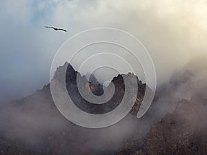 Horror mountain shadows. Dramatic fog among giant rocky mountains. Ghostly atmospheric view to big cliff in cloudy sky. Low clouds