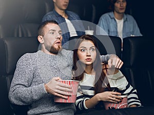 Young scared couple watching thriller in cinema