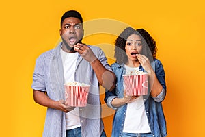 Horror Movie. Shocked african american couple with popcorn buckets over yellow background