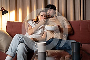 Horror Movie. Shocked couple watching scary film on tv and eating popcorn at home