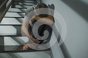 Horror movie style portrait of sad and desperate man suffering depression problem or mental disorder sitting on staircase at home