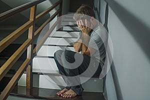 Horror movie style portrait of sad and desperate man suffering depression problem or mental disorder sitting on staircase at home