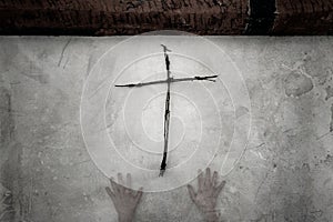 A horror spooky concept. A wooden cross made out of twigs, hanging on a white wall, with two ghostly, transparent hands coming up