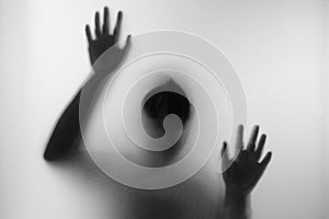 Horror woman behind the matte glass in black and white. Blurry hand and body figure abstraction.Halloween background.Black and