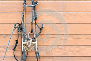 Horse bridle with decoration hanging on stable wooden wall.