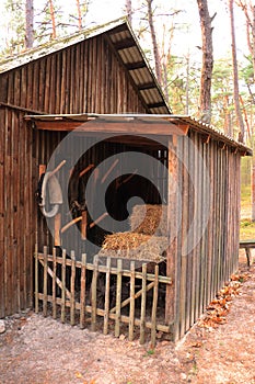 Horse collars and dry hay bales in an open annex by a wooden shed