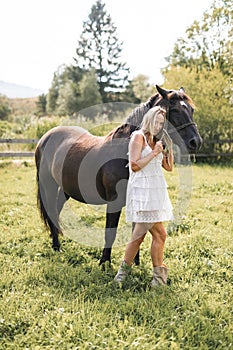 Horse and girl outdoors. Lovely stylish cowgirl with her horse on a ranch. Beautiful girl in white short boho dress with