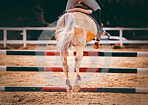 A horse leaping over a barrier at an equestrian competition, seen from behind. The horse riding. The achievement in equestrian