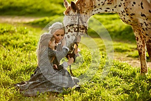 Horse and little girl cuddle with the woman, summer background with green grass