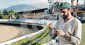 Horse racing. The man bet on a horse with a smartphone. Young man uses a smartphone on a racetrack. The bookmaker wins