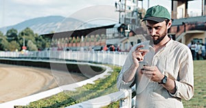 Horse racing. The man bet on a horse with a smartphone. Young man uses a smartphone on a racetrack. The bookmaker wins